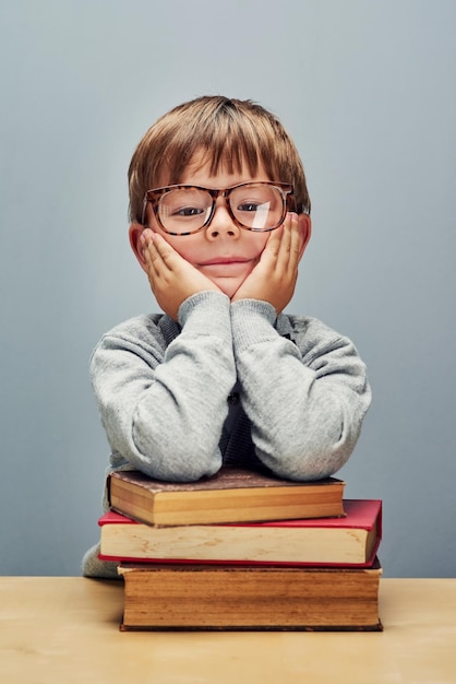 Costruire il suo futuro su una base di libri Ritratto in studio di un ragazzino intelligente che si appoggia su una pila di libri su uno sfondo grigio