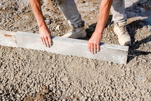 Costruttore che posiziona il cordolo del perno di bordatura su calcestruzzo semisecco utilizzando una linea di corda per tenerli dritti