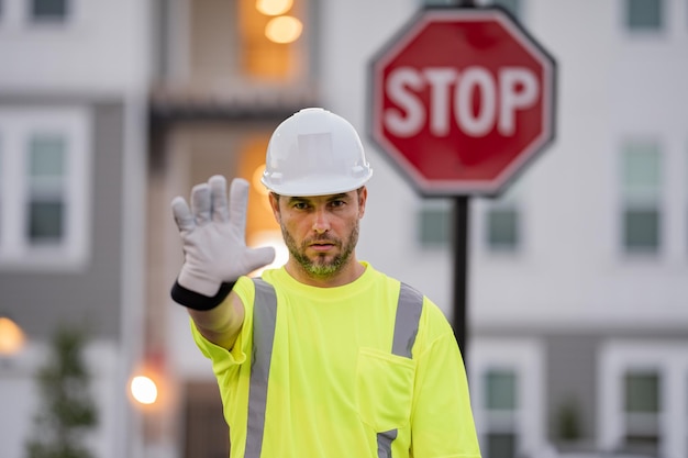 Costruttore con gesto di arresto nessuna mano pericolosa sul concetto di costruzione uomo nel casco che mostra il segnale stradale di stop