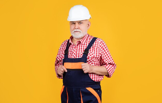 Costruttore di uomo anziano serio in casco su sfondo giallo
