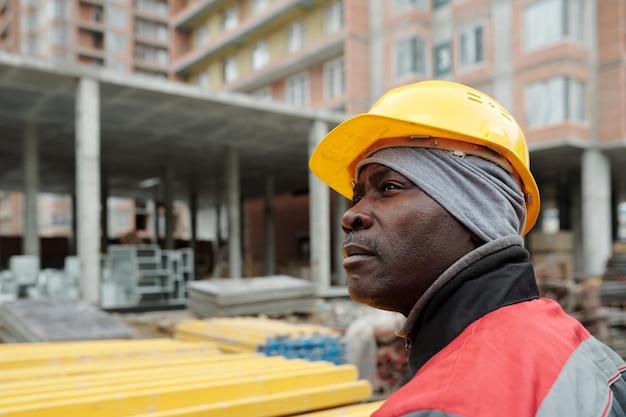 Costruttore maschio afroamericano in abiti da lavoro ed elmetto protettivo che guarda da parte