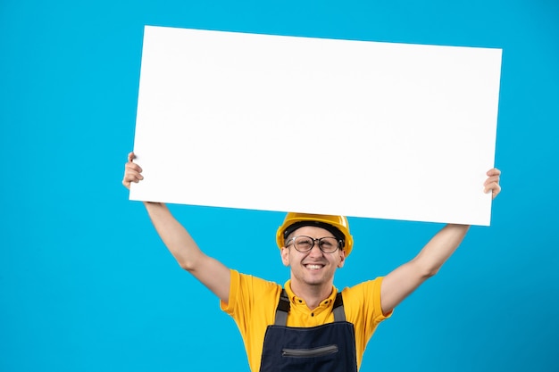 Costruttore maschio emotivo di vista frontale in uniforme con piano di carta sull'azzurro