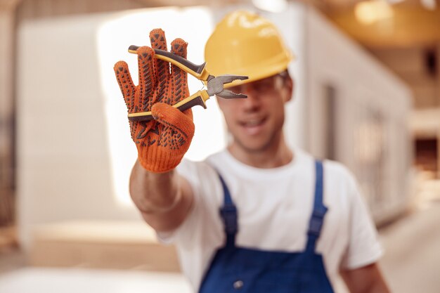 Costruttore maschio mano nei guanti da lavoro che tengono le pinze