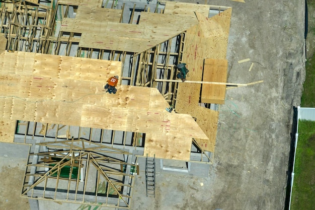 Costruttori che lavorano alla costruzione del tetto di una casa residenziale incompiuta con struttura a telaio in legno nell'area suburbana della Florida Concetto di sviluppo abitativo