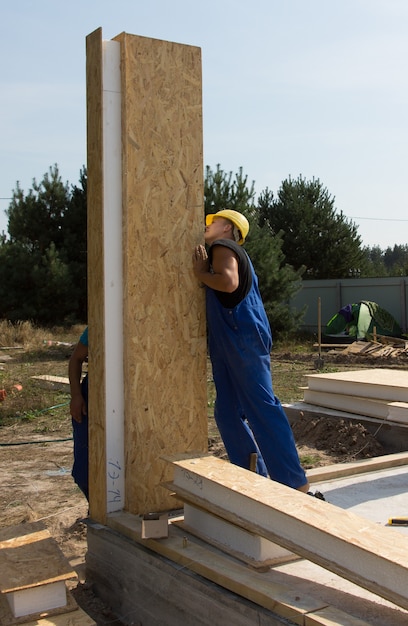 Costruttori che posizionano un pannello a parete verticale con uno spesso isolamento in un cantiere per una nuova casa di costruzione