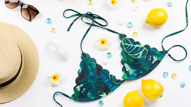 Costume da bagno bikini donna con cappello di paglia, fiori e frutti, spazio di copia. Concetto di viaggio