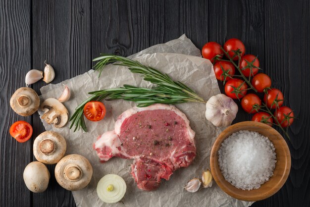 Cotoletta cruda del porco con le spezie e gli ingredienti per la griglia o cucinando sulla superficie di legno