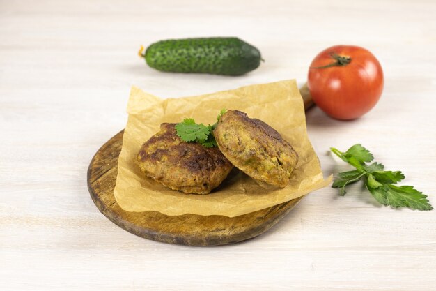 Cotoletta di hamburger di carne di manzo fatta in casa sul tagliere, carta da forno sul tavolo bianco con verdure, erbe. Concetto di dieta a basso contenuto di carboidrati. Avvicinamento. Messa a fuoco selettiva. Copia spazio