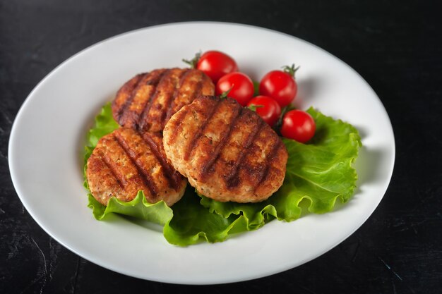 Cotoletta fritta con lattuga e pomodori in un piatto bianco su sfondo nero