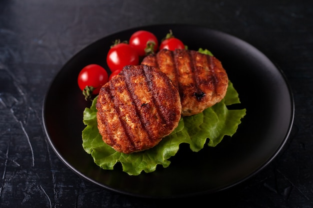 Cotoletta fritta con lattuga e pomodori in un piatto nero su sfondo nero