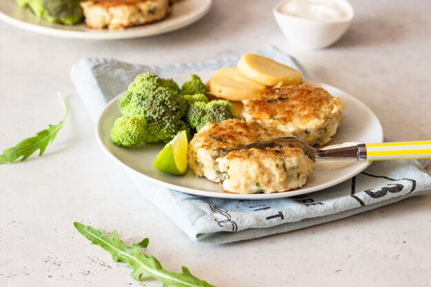 Cotolette deliziose (pesce o carne) con broccoli, patate e salsa su un piatto.