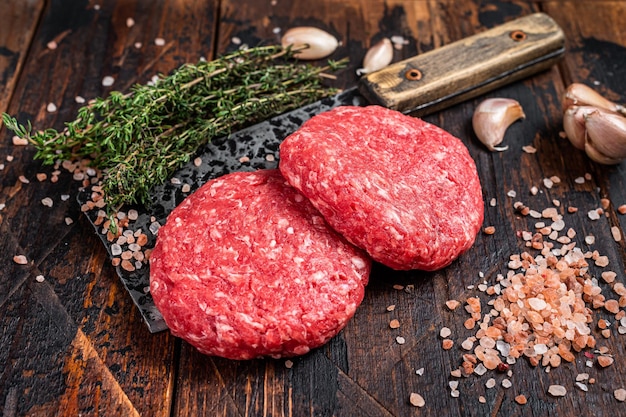 Cotolette di bistecca cruda con carne di manzo tritata su una mannaia da macellaio. Fondo in legno. Vista dall'alto.