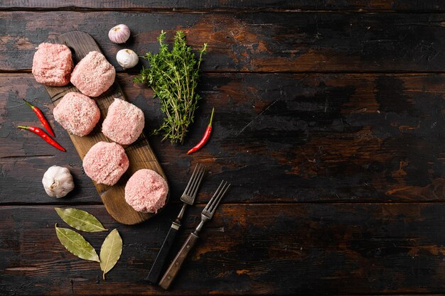 Cotolette di bistecca di carne di manzo macinata cruda su un vecchio sfondo di tavolo in legno scuro vista dall'alto piatto con spazio di copia per il testo