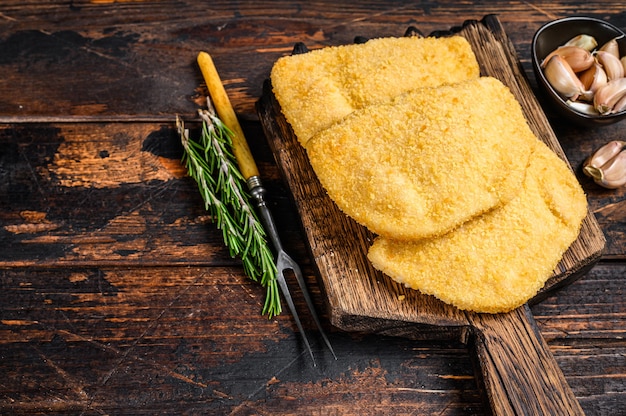 Cotolette di carne cordon bleu di pollo crudo con briciole di pane su una tavola di legno. Fondo in legno scuro. Vista dall'alto. Copia spazio.