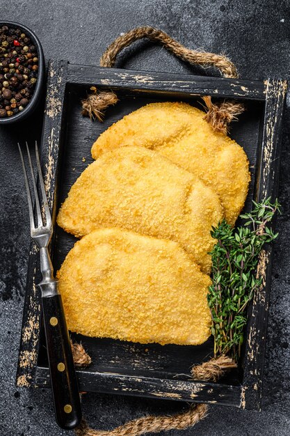 Cotolette di carne di cordon bleu di pollo crudo in un vassoio di legno con erbe aromatiche.