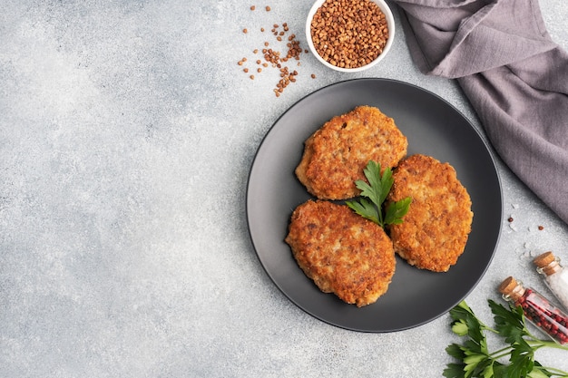 Cotolette di grano saraceno con formaggio e prezzemolo su un piatto su fondo grigio chiaro