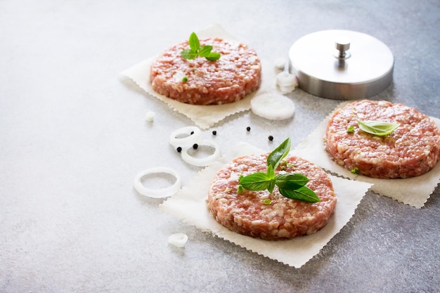 Cotolette di hamburger crudi di carne di manzo biologica con spezie e basilico su una vista dall'alto di sfondo in pietra o ardesia con spazio per la copia