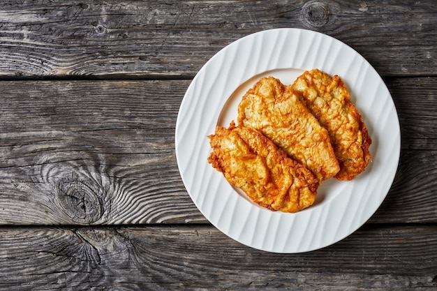 Cotolette di petto di pollo disossate fritte in padella servite su una piastra bianca su una tavola in legno rustico, vista panoramica dall'alto, piatto laico, spazio libero, close-up