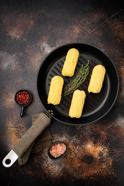 Cotolette di pollo fresche preparate per il set di frittura, sulla padella in ghisa, sul vecchio sfondo rustico scuro della tavola, vista dall'alto piatta