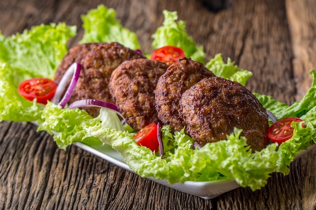 Cotolette di polpette di hamburger di manzo con insalata di lattuga pomodoro cipolla su tavola di legno.