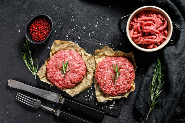 Cotolette e condimenti crudi di carne di manzo macinata di manzo. Fattoria biologica di carne. Sfondo nero. Vista dall'alto