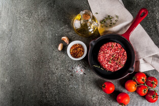 Cotolette organiche crude degli hamburger della carne del manzo con le spezie, timo, pomodori, olio d'oliva in padella sul copyspace nero e di vista superiore