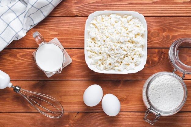 Cottura degli ingredienti su un tavolo di legno marrone per cucinare. Uova, farina, ricotta e latte su una tavola, sfondo alimentare. Vista dall'alto, piatto.