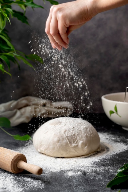 Cottura del pane fatto in casa con lievito naturale. Setacciare la farina sulla pasta di pane cruda sul tavolo, sfondo scuro, fuoco selettivo.