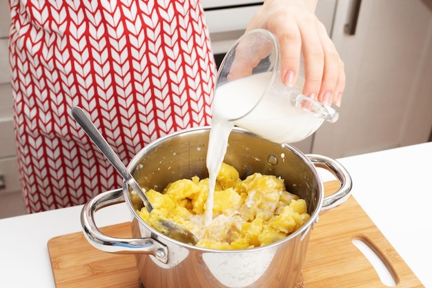 Cottura del purè di patate Le mani femminili aggiungono il latte alla padella