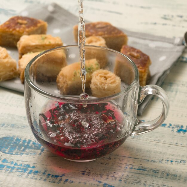 Cottura del tè alla frutta Versando acqua bollente in una tazza sullo sfondo di dolci orientali