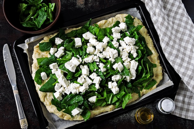 Cottura della pizza con spinaci di feta. Pizza Keto. Pizza cruda degli spinaci della feta su uno strato per cuocere. Disteso.