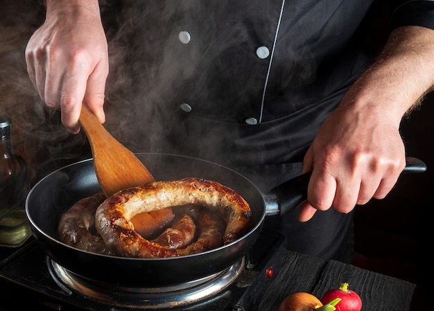 Cottura della salsiccia di carne nella cucina del ristorante Cuoco o chef frigge la salsiccia in una padella
