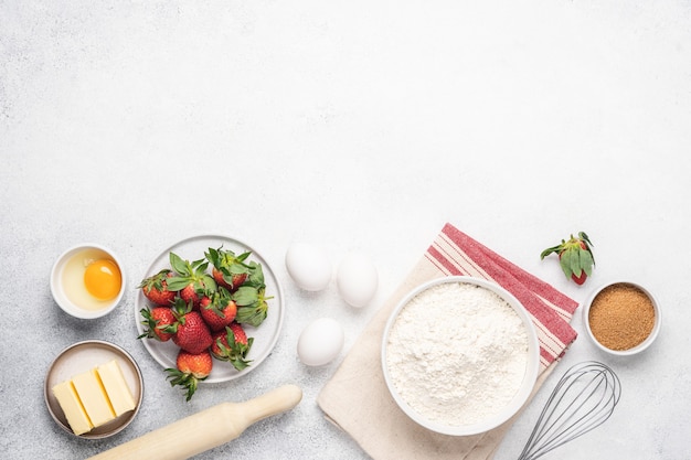 Cottura torta di fragole sfondo bianco. Farina, burro, uova e utensili da cucina sul tavolo di pietra bianca