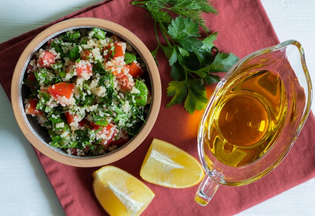 Cous cous con prezzemolo, pomodoro, limone e olio d'oliva Insalata araba tradizionale Tabbouleh su sfondo bianco con tessuti rossi Vista dall'alto