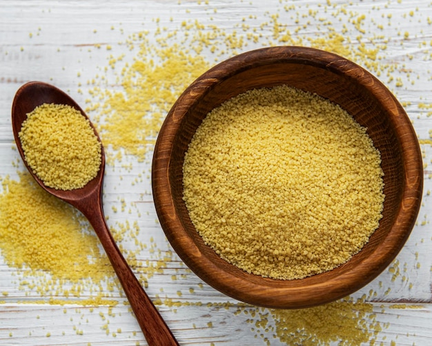 Cous cous crudo in una ciotola di legno e cucchiaio sul tavolo