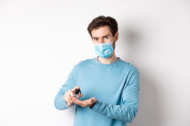 Covid-19, concetto di salute e quarantena. Uomo caucasico in maschera medica utilizzando disinfettante per le mani, applicare l'antisettico dalla diffusione del coronavirus, sfondo bianco.