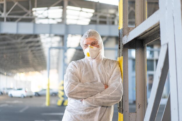 COVID-19 coronavirus medico in piedi parcheggio ospedaliero vestito tuta protettiva bianca tuta ignifuga. Malattia infettiva pandemica lavoratore medico in prima linea, scoppio. Tiro medio di operatore medico maschio