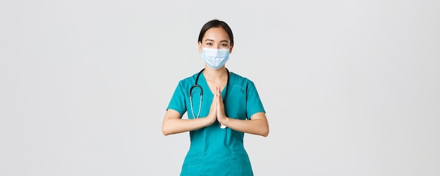 Covid-19, malattia da coronavirus, concetto di operatori sanitari. Il medico asiatico sorridente speranzoso, il medico in maschera medica e scrub si tengono per mano in un gesto di preghiera, ringraziando, sfondo bianco.