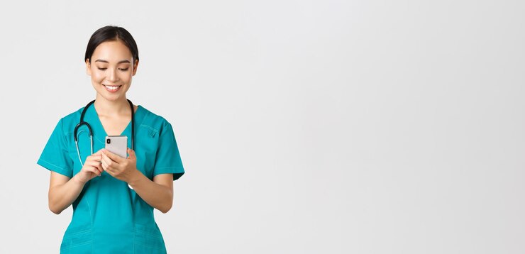 Covid-19, operatori sanitari e prevenzione del concetto di virus. Sorridente felice bella stagista asiatica femminile, medico che effettua una telefonata, guardando lo schermo del telefono cellulare soddisfatto, messaggiando o utilizzando l'app.