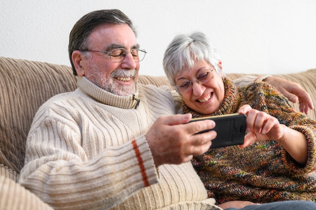 Covid-19 resta a casa. Felice coppia di anziani in pensione, facendo una videochiamata di famiglia con il cellulare. Distanziamento sociale, espressione positiva.