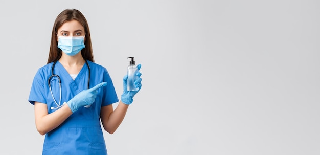 Covid19 prevenzione del virus operatori sanitari sanitari e concetto di quarantena Giovane infermiera o dottoressa professionista in maschera medica scrub blu che punta il dito contro il disinfettante per le mani