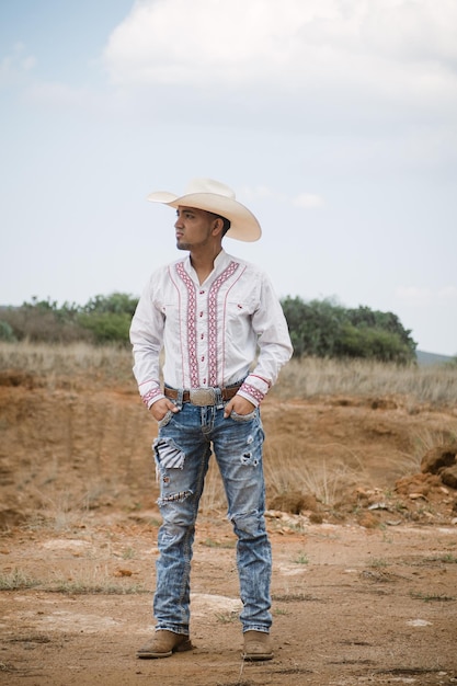 Cowboy che indossa jeans e un cappello in piedi sotto il cielo con soffici nuvole che lavorano in una fattoria