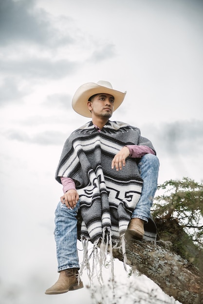 Cowboy che indossa un poncho seduto sotto un albero nel cielo