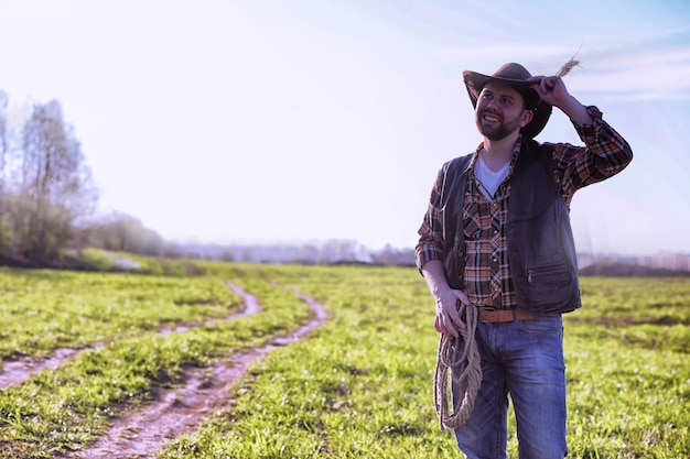 Cowboy con un cappello e un lazo in piedi in un campo al tramonto