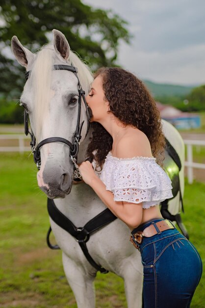cowgirl con i capelli ricci che bacia il suo cavallo bianco