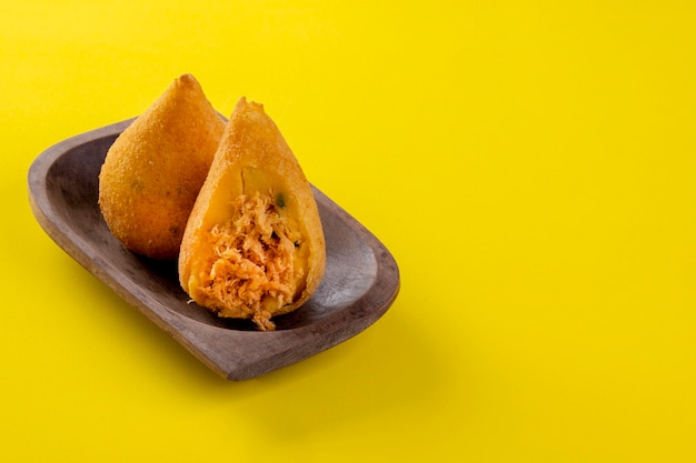 Coxinha fritto in contenitore di legno su sfondo giallo.