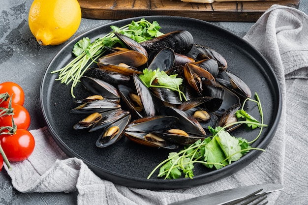 Cozze bollite in salsa di aglio con prezzemolo e ingredienti, su piatto, su sfondo grigio