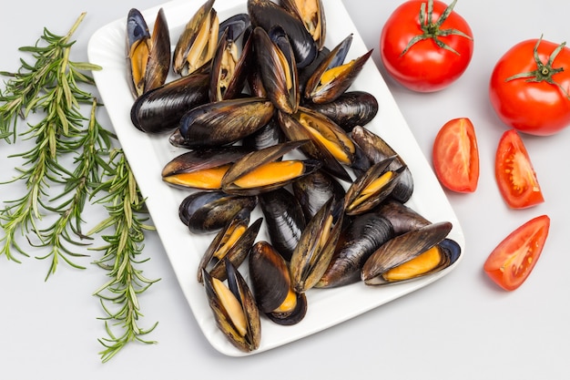 Cozze con gusci aperti sul piatto bianco. Rosmarino e pomodori sul tavolo. Lay piatto.