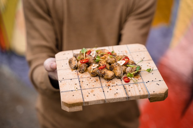Cozze fritte con peperoncino, aglio, sesamo, erbe aromatiche, su tavola di legno quadrata. Servire il piatto dal cameriere.