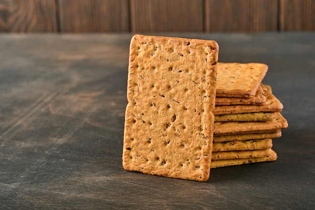 Cracker con semi di lino e crusca d'avena di forma rettangolare sul tavolo di legno scuro. Spuntino per una corretta alimentazione.